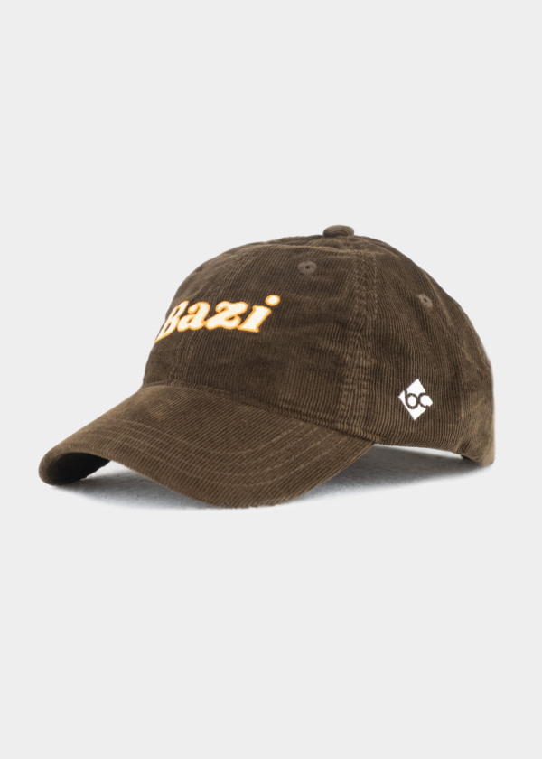 Braune Cord-Cap mit gebogenem Schirm. Auf der Vorderseite ist der Schriftzug "Bazi" in weißer Schrift und orangener Umrandung gestickt, seitlich befindet sich ein kleines weißes Logo mit den Buchstaben "bc"