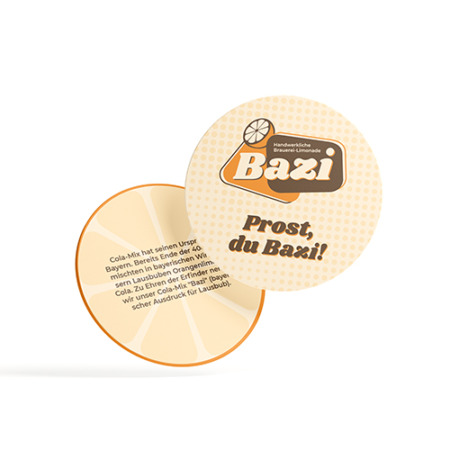 Zwei runde Bazi-Bierdeckel: einer mit dem Schriftzug "Prost, du Bazi!" und dem Logo der Marke Bazi, der andere mit einer kurzen Beschreibung zur Herkunft von Bazi Cola-Mix. Design in frischen Orangetönen mit Zitronenmotiv im Hintergrund.
